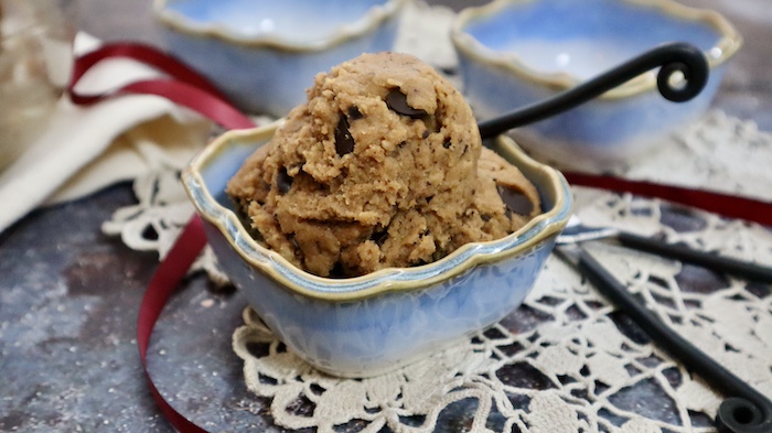 This is a photo of a light blue ceramic square bowl filled with dairy and gluten free chickpea cookie dough with three black handled spoons all on a lacy cloth.