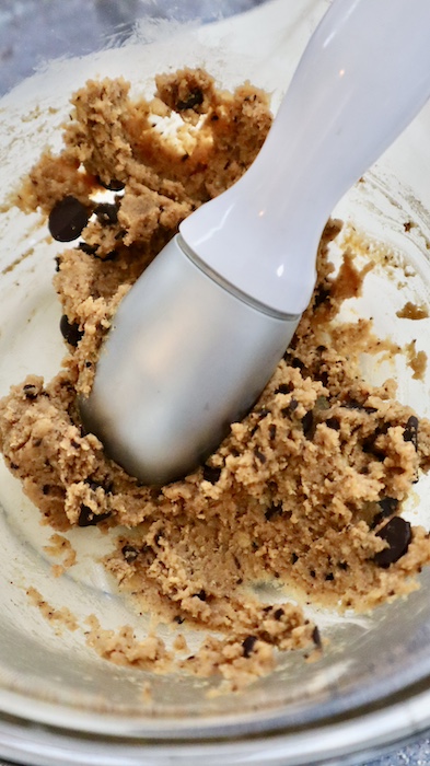 This is a photo of an ice cream scoop scooping out dairy and gluten free chickpea cookie dough from a clear glass bowl. 