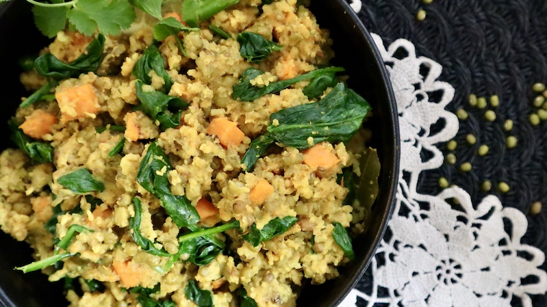 with easy vegan green kitchari detox bowl on a white doily and black round table mat and dried mung beans scattered near the bowl. 