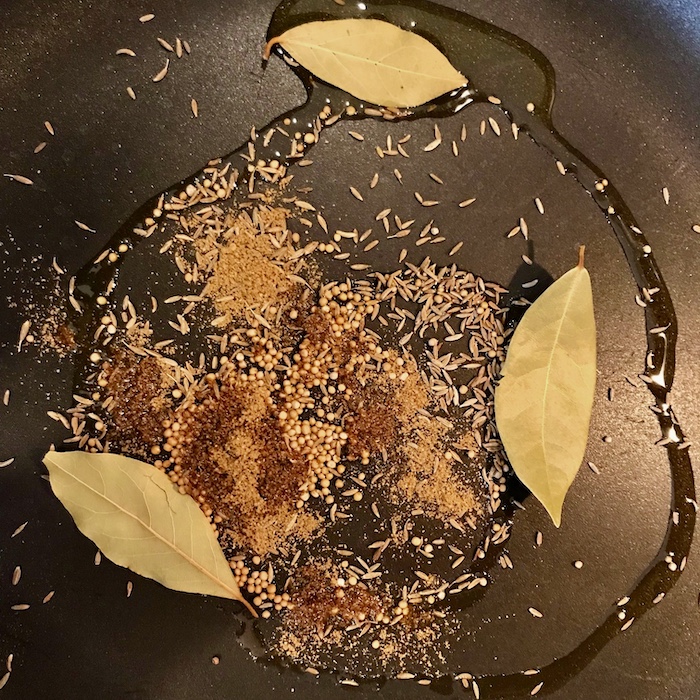 This is a photo of a skillet with oil and spices and bay leaves in it.