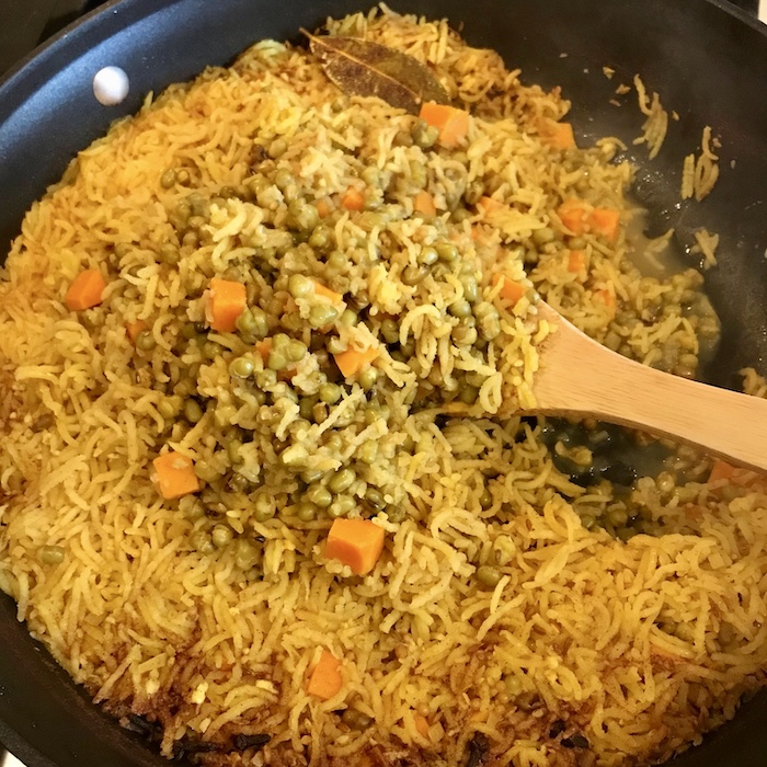 This is a photo of cooked kitchari in a large skillet with a wooden spoon in it. 